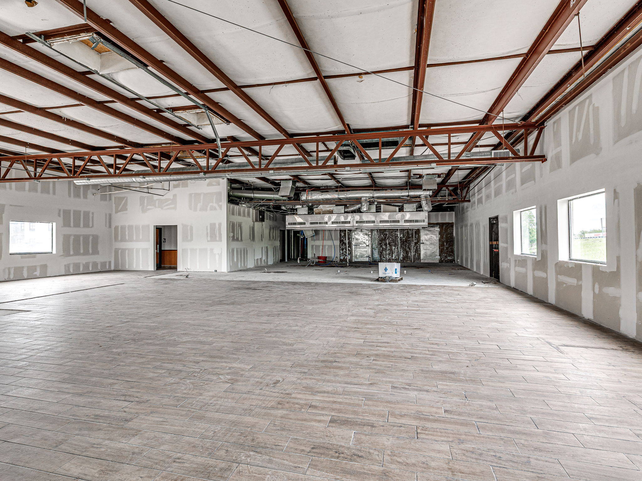 Open white-boxed interior with exposed steel joists, ductwork and new tile floor